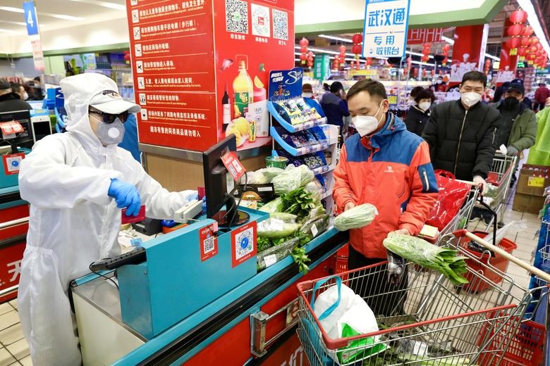 A worker in protective suit serves customers at a checkout counter of a supermarket in Wuhan